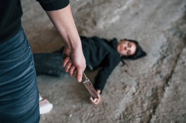 Murderer with knife covered in blood standing near his dead female young victim.