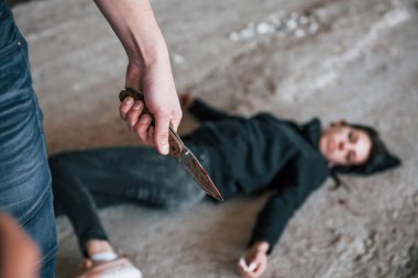 Murderer with knife covered in blood standing near his dead female young victim.