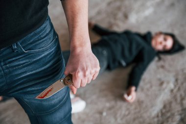 Murderer with knife covered in blood standing near his dead female young victim.