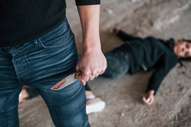 Murderer with knife covered in blood standing near his dead female young victim.