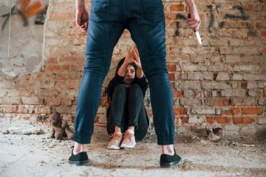 Violent man standing with knife in hand and threatens girl that sits on the floor in abandoned building.
