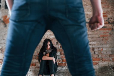 Violent man standing and threatens girl that sits on the floor with teddy bear in abandoned building.