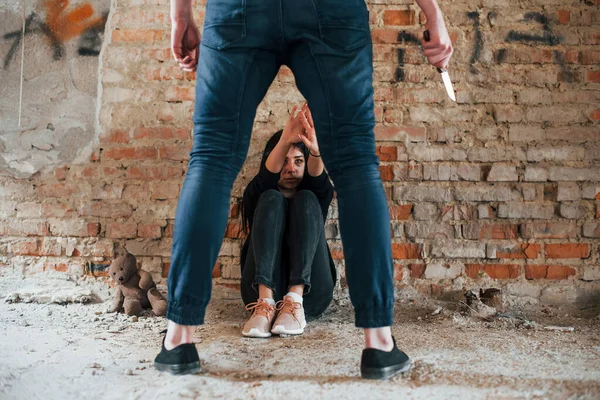 暴力的な男立っているナイフで手と脅迫女の子それに座っている床の上に放棄された建物 — ストック写真