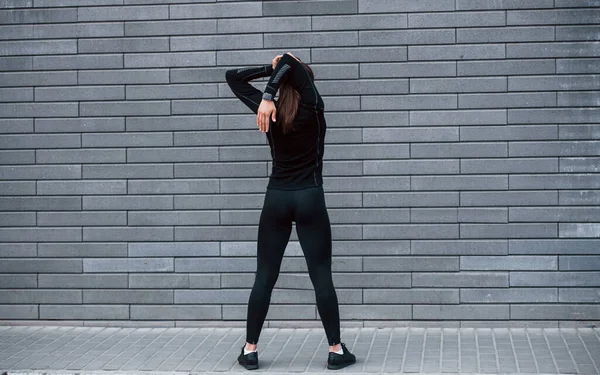 穿着黑色运动服的年轻女运动员站在灰色墙边的后视镜 — 图库照片