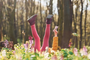 Gündüz vakti Bahar Ormanı 'nda yerde uzanan günlük giysiler içinde mutlu küçük kız..