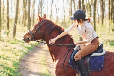 Güneşli bir günde atıyla birlikte ormanda koruyucu şapkalı genç bir kadın..