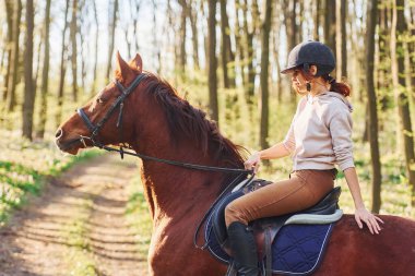 Güneşli bir günde atıyla birlikte ormanda koruyucu şapkalı genç bir kadın..