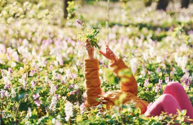 Gündüz vakti Bahar Ormanı 'nda yerde uzanan günlük giysiler içinde mutlu küçük kız..
