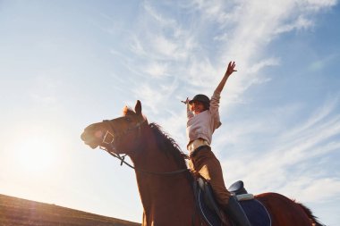 Güneşli bir günde atıyla birlikte tarım alanında koruyucu şapkalı genç bir kadın..