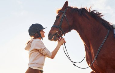 Genç bir kadın atıyla güneşli bir günde tarım alanında dikiliyor..