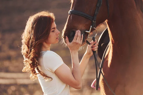 Genç bir kadın atıyla güneşli bir günde tarım alanında dikiliyor..