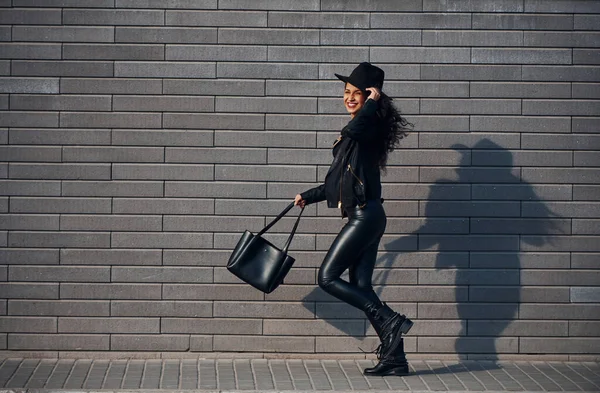 巻き毛と黒の服で美しいブルネットは壁の近くに屋外で歩いています — ストック写真