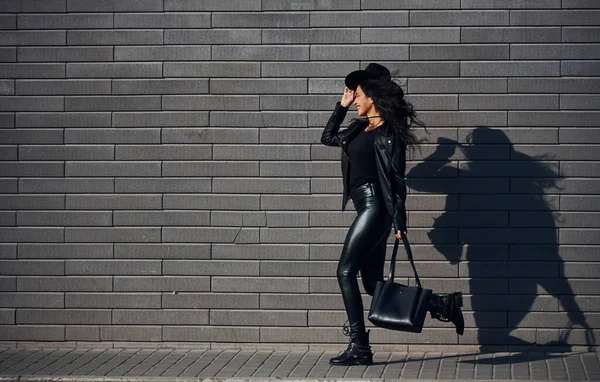 Kıvırcık Saçlı Siyah Elbiseli Güzel Bir Esmer Duvarın Yanında Yürür — Stok fotoğraf
