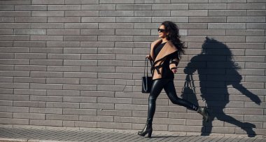 Güzel esmer, kıvırcık saçlı, siyah elbiseli, duvarın yanında koşan..