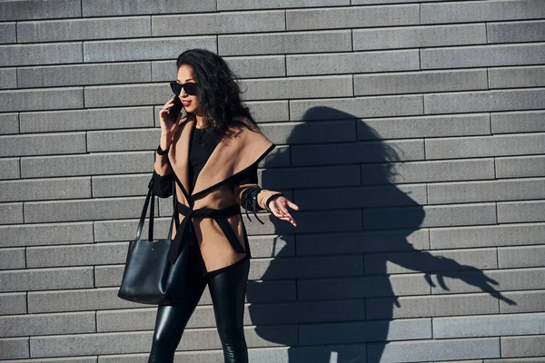 Güzel Esmer Kıvırcık Saçlı Siyah Elbiseli Dışarıda Duvarın Yanında Telefonla — Stok fotoğraf