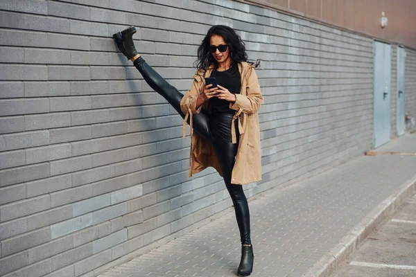 Kıvırcık Saçlı Siyah Elbiseli Güzel Esmer Bacaklarını Duvarın Yakınına Uzatıyor — Stok fotoğraf