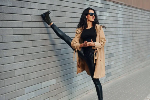 Kıvırcık Saçlı Siyah Elbiseli Güzel Esmer Bacaklarını Duvarın Yakınına Uzatıyor — Stok fotoğraf