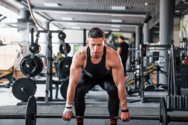 Lifting barbell. Young sportive strong man in black wear have workout day in gym.