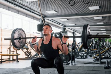 Lifting barbell. Young sportive strong man in black wear have workout day in gym.