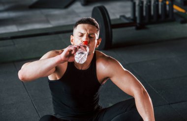Mola verip su içiyorum. Siyah elbiseli genç sporcu güçlü adam spor salonunda antrenman yapıyor..