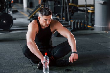 Mola verip su içiyorum. Siyah elbiseli genç sporcu güçlü adam spor salonunda antrenman yapıyor..