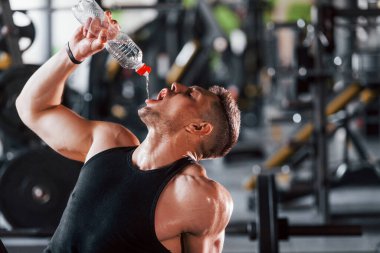 Mola verip su içiyorum. Siyah elbiseli genç sporcu güçlü adam spor salonunda antrenman yapıyor..