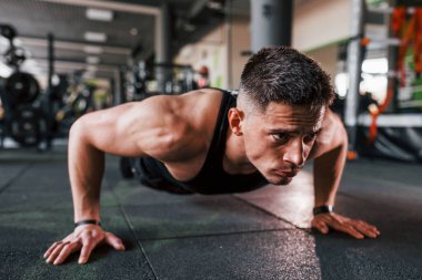 Şınav çekiyorum. Siyah elbiseli genç sporcu güçlü adam spor salonunda antrenman yapıyor..