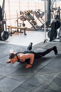 Şınav çekiyorum. Siyah elbiseli genç sporcu güçlü adam spor salonunda antrenman yapıyor..
