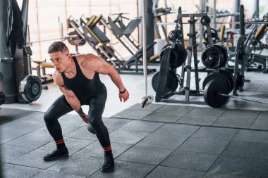 Kilo vermek. Siyah elbiseli genç sporcu güçlü adam spor salonunda antrenman yapıyor..