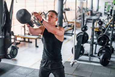 Liting weight. Young sportive strong man in black wear have workout day in gym.