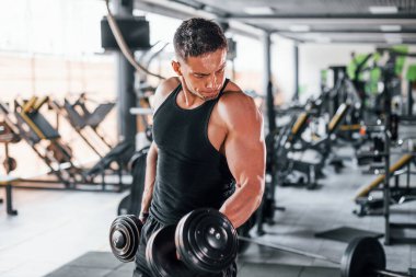 Dambılları yakmak. Siyah elbiseli genç sporcu güçlü adam spor salonunda antrenman yapıyor..