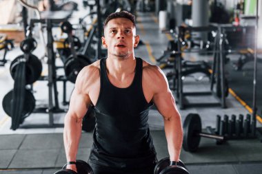 Dambılları yakmak. Siyah elbiseli genç sporcu güçlü adam spor salonunda antrenman yapıyor..