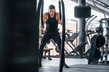 Düğümlerle egzersiz yapmak. Siyah elbiseli genç sporcu güçlü adam spor salonunda antrenman yapıyor..