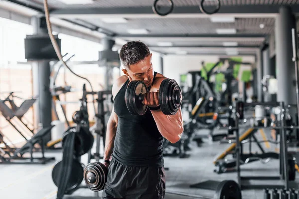 Dambılları yakmak. Siyah elbiseli genç sporcu güçlü adam spor salonunda antrenman yapıyor..