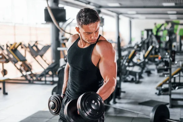 Dambılları yakmak. Siyah elbiseli genç sporcu güçlü adam spor salonunda antrenman yapıyor..