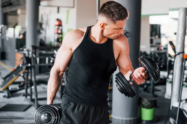 Dambılları yakmak. Siyah elbiseli genç sporcu güçlü adam spor salonunda antrenman yapıyor..