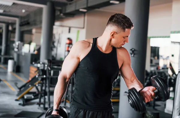 Dambılları yakmak. Siyah elbiseli genç sporcu güçlü adam spor salonunda antrenman yapıyor..