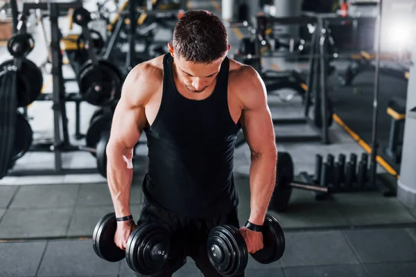 Dambılları yakmak. Siyah elbiseli genç sporcu güçlü adam spor salonunda antrenman yapıyor..