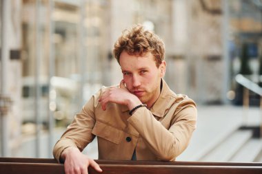 Şehrin dışındaki ahşap çitlere yaslanan resmi klas elbiseli zarif genç adam..