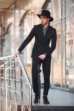 Siyah şapkalı, açık havada şemsiyesi olan zarif bir genç..