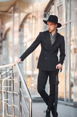 Elegant young man in black hat and with umbrella outdoors in the city.