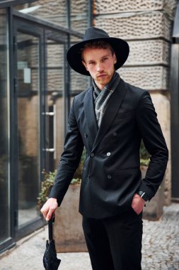 Siyah şapkalı, elinde şemsiyesi olan şık bir genç adam..