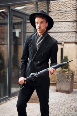 Siyah şapkalı, elinde şemsiyesi olan şık bir genç adam..