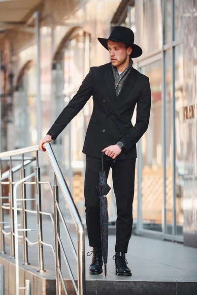 Siyah şapkalı, açık havada şemsiyesi olan zarif bir genç..