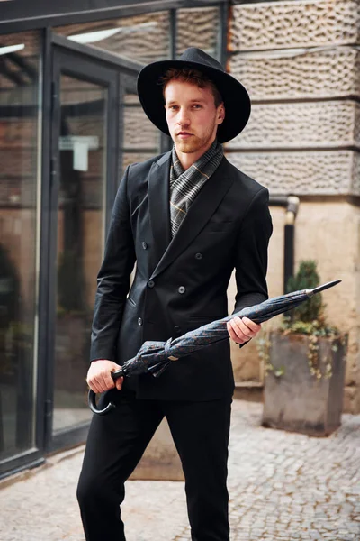 Siyah şapkalı, elinde şemsiyesi olan şık bir genç adam..