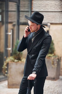 Telefonla konuşuyorum. Siyah şapkalı, elinde şemsiyesi olan şık bir genç adam..