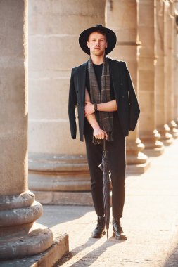 Siyah şapkalı, elinde şemsiyesi olan şık bir genç adam..