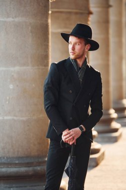 Siyah şapkalı, elinde şemsiyesi olan şık bir genç adam..