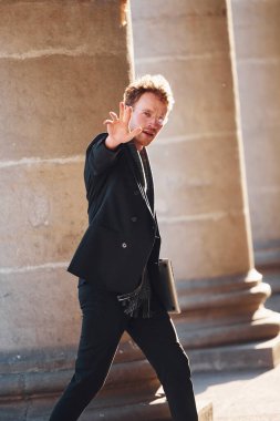 Ellerinde dizüstü bilgisayarla. Gözlüklü zarif genç adam şehrin dışında şık kıyafetler giyiyor..