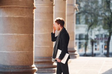 Ellerinde dizüstü bilgisayarla. Gözlüklü zarif genç adam şehrin dışında şık kıyafetler giyiyor..